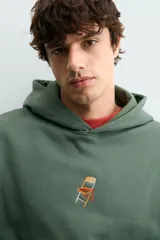 Sudadera con capucha de corte relajado, color verde oscuro, con interior perchado y bordado pequeño de una silla en el centro del pecho.