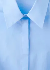Camisa de popelín celeste con cuello camisero, manga larga y cierre delantero con botones.