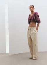 Blusa crop de color bordó, con diseño elástico fruncido, cuello redondo y mangas cortas abullonadas con lazo ajustable en los puños.
