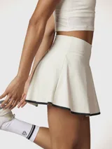 Falda skort deportiva de tiro alto, color blanco con borde inferior en contraste negro. Incluye short integrado con bolsillo lateral.
