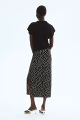 Pollera midi negra con estampado de lunares blancos, tiro alto, cintura elástica con fruncidos laterales y abertura pronunciada en un lateral.