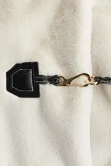 Campera de tejido suave efecto peluche en color crudo, con cuello redondo, hombros caídos y cierre frontal mediante alamares con detalles en contraste negro. Cuenta con bolsillos laterales ribeteados y forro interior.