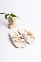 Sandalias bajas color crudo con dos tiras y hebillas doradas.