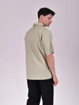 Camisa de manga corta en color blanco, con cuello clásico y cierre frontal oculto mediante botones. Presenta un diseño minimalista de corte recto.