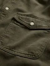 Camisa de jean de corte clásico en color azul oscuro, con cierre frontal de botones, cuello camisero y dos bolsillos frontales con solapa y botón.