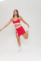 Conjunto deportivo de dos piezas color rojo con detalles en blanco. Incluye un top deportivo con cuello redondo y elástico inferior con logo, y una pollera short con tajo frontal.