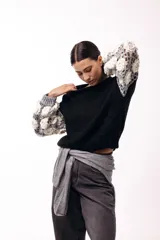 Sweater de punto con cuerpo liso en color negro y mangas largas tejidas en crochet gris con aplicaciones de flores en relieve color blanco.