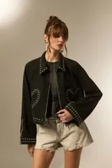 Campera cropped de jean color negro, con cuello camisero, cierre frontal y detalles de tachas plateadas en el cuello, hombros, mangas y ruedo. Presenta un diseño de tachas en forma de corazón en el pecho.