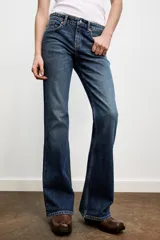 Jeans de tiro bajo con diseño bootcut, cinco bolsillos y trabillas para cinturón. Presenta un acabado flare en el bajo y cierre frontal con cremallera y botón metálico.
