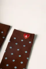 Medias largas color marrón con estampado de lunares celestes. Tienen un corazón rojo bordado con la letra 'R' en blanco en la parte superior y la palabra 'Rotunda' en rojo en el lateral del pie.