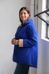 Tapado de paño color azul con capucha, cierre frontal y detalles en color beige en el interior de la capucha, puños y bordes de los bolsillos.