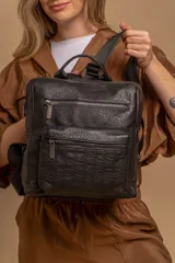 Mochila mediana de cuero sintético con textura rugosa, cuenta con dos compartimentos frontales con cierre, asa superior y correas ajustables.