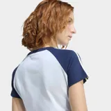Remera Adidas de ajuste ceñido, color celeste claro con mangas cortas en azul marino y las icónicas tres rayas blancas en los hombros. Presenta cuello redondo acanalado y el logo del trébol bordado en el pecho.