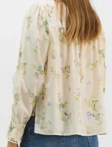 Blusa de algodón con estampado floral de flores silvestres sobre fondo claro. Presenta cuello redondo con detalle de puntilla, abotonadura frontal, canesú con frunces y mangas largas con puños elásticos decorados con puntilla.