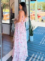 Vestido largo tipo solera, con escote en V profundo y tirantes finos. Presenta un estampado paisley en tonos rosados, lilas y blancos, con ajuste de lazo en la cintura y volados en el ruedo.