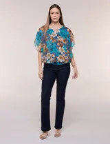 Blusa de gasa semitransparente con hilos de lúrex, diseño estampado floral en tonos blanco, gris y negro, silueta holgada tipo capa y escote redondo con detalle metálico.