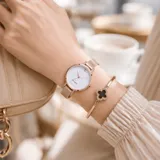 Reloj analógico de mujer con caja redonda de metal en tono oro rosa, esfera blanca con acabado brillante y malla metálica ajustable. Diseño minimalista y elegante.