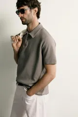 Remera polo regular fit de color gris oscuro, confeccionada en tejido de algodón con textura de rayas verticales. Cuenta con cuello solapa, cierre frontal con botones y mangas cortas con terminación en rib.
