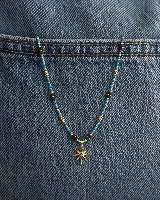 Collar de cuentas turquesas con detalles en dorado y cuentas cúbicas de color marrón oscuro, con un dije central en forma de estrella de ocho puntas con una piedra turquesa en el centro.