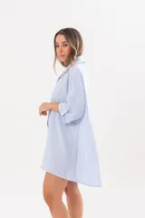 Vestido camisero de lino color celeste, con escote en V, cuello clásico, cierre frontal de botones y mangas tres cuartos regulables. Diseño holgado con corte asimétrico.