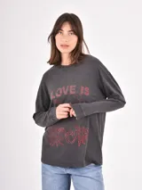 Remera de manga larga en color azul piedra con efecto lavado. Presenta estampado gráfico en las mangas con la frase 'BROKEN HEART' y un diseño floral en la manga derecha.