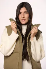 Chaleco puffer de nylon en color verde oliva, con cuello alto, cierre frontal con cremallera y botones a presión, y bolsillos laterales.