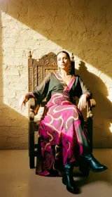 Vestido largo de tul translúcido con estampado de líneas orgánicas en tonos magenta, vino y dorado, escote cruzado y mangas amplias.