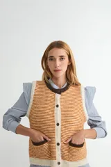 Chaleco de punto con diseño de rayas horizontales en tonos naranja y crema, con cuello redondo, cierre frontal de botones y dos bolsillos delanteros con bordes en color marrón oscuro.