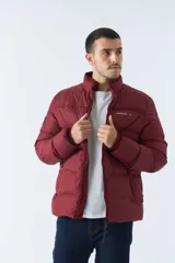 Campera puffer color bordó, con cuello alto y cierre frontal. Tiene bolsillos laterales con cierre y logo estampado en el pecho.