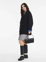 Cartera tipo shoulder bag de cuero liso color negro, con solapa frontal y cierre metálico con logo grabado. Posee una correa ajustable para llevar al hombro.