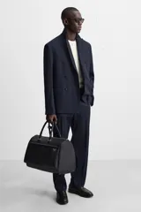 Bolso de viaje negro con textura grabada, compartimento principal con cierre de cremallera, bolsillo interior con cremallera, bolsillo frontal con cremallera y asa de hombro removible y ajustable.