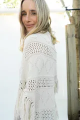 Poncho de tejido de algodón color beige claro, con diseño de punto calado y flecos en el borde inferior.