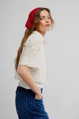 Camisa crop de encaje floral semitransparente, color blanco, con mangas cortas y ribetes en color contrastante.