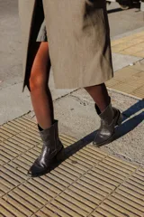 Bota corta estilo tejano de cuero negro, con taco cuadrado y punta cuadrada. Presenta costuras decorativas en el empeine y cierre lateral.