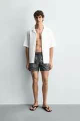 Bañador de hombre de tejido técnico, color gris oscuro con estampado abstracto en tonos más claros. Presenta cintura elástica ajustable con cordón, bolsillos laterales y un bolsillo trasero de plastrón.