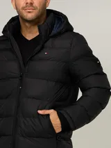 Campera puffer Tommy Hilfiger de color negro, acolchada con diseño horizontal, capucha integrada y cierre frontal de cremallera. Cuenta con bolsillos laterales con cierre y el logo bordado en el pecho.