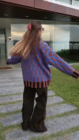 Buzo tipo saco abotonado con diseño de cuadros en tonos marrones y beige, corte recto y oversize. Presenta cuello camisero, cierre frontal con botones personalizados y dos bolsillos delanteros.