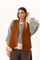 Chaleco oversize confeccionado en cuero descarne, con diseño de terminación en picos, detalle de tachas metálicas en los bordes frontales y flecos en la espalda.