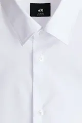 Camisa de vestir blanca con cuello inglés, tapeta clásica y corte ajustado. Presenta mangas largas con puños abotonados y bajo levemente redondeado.