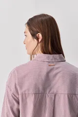 Camisa de calce relajado con diseño a rayas verticales en tonos azul y blanco, cuello clásico, mangas largas con puños abotonados y cierre frontal con botones. Presenta bolsillos aplicados en el delantero y una silueta versátil.