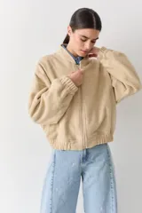 Campera bomber de paño color beige, con cierre frontal, cuello alto y puños elásticos.
