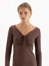 Top de manga larga color violeta, con escote en V y detalle de fruncido central regulable mediante lazos finos en el delantero. Presenta un ajuste entallado al cuerpo.