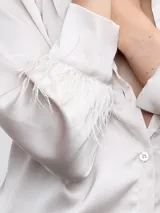Camisa color beige de raso con cuello clásico, cierre frontal con botones y mangas largas con puños adornados con plumas.