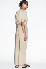 Mono largo de cuello solapa y escote en pico cruzado, con mangas cortas. Presenta bolsillos laterales de plastrón con solapa y botones, y un cinturón del mismo tejido para ajustar en la cintura. Cierre frontal con cremallera y botón interior.