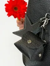 Cartera tote de cuero genuino color negro, con costuras visibles a contratono, asas dobles para hombro, parche frontal con logo grabado y charms colgantes en forma de estrella y mini monedero.
