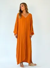 Vestido largo color amarillo, de corte amplio, con escote en V y mangas largas con detalle de flecos. Presenta aberturas laterales en el ruedo.