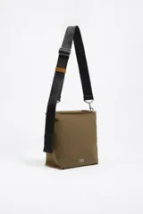 Bolso bandolera de tamaño pequeño en color verde oliva, confeccionado en poliamida con detalles en piel vacuna. Cuenta con asa larga regulable de tejido en color negro, cierre superior con cremallera y logo de la marca estampado en la parte frontal.