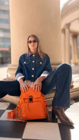 Mochila de nylon color naranja, con tapa superior y cierre de broche, bolsillo frontal con cierre y bolsillos laterales. Incluye correas regulables para la espalda y asa de mano.