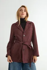 Chaqueta de gamuza sintética color bordó, con cuello solapa, cierre frontal de botones y cinturón ajustable del mismo material. Posee bolsillos frontales y mangas largas.