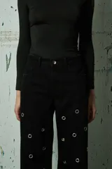 Jean de corte recto y tiro medio, color negro, con diseño de ojales metálicos distribuidos por toda la prenda.